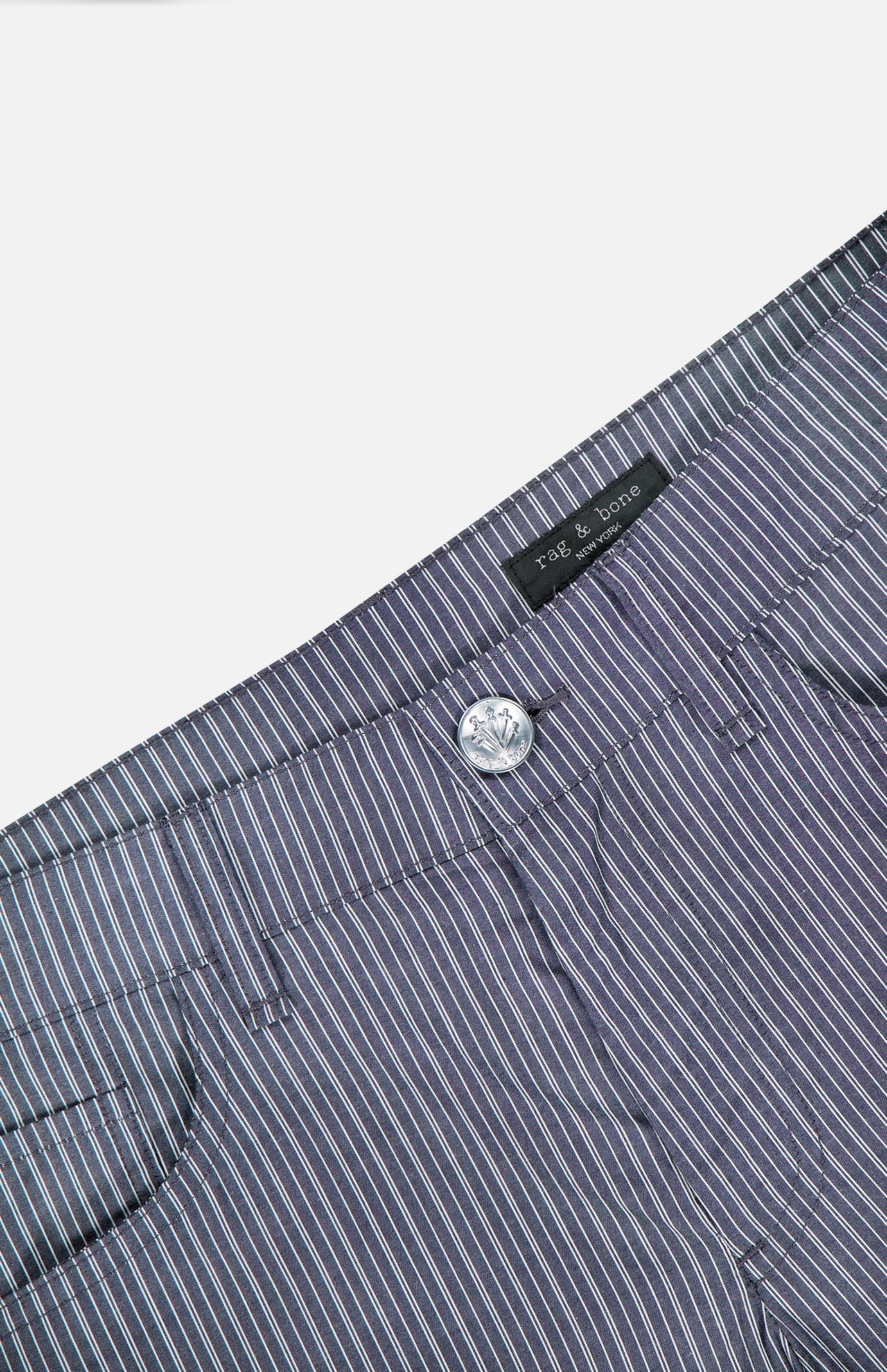 Close-up of the waistband and upper section of RAG & BONE's Saige Stripe Poplin Pant in lightweight cotton, featuring blue, white, and pink stripes, front button closure, belt loops, and an interior brand label.