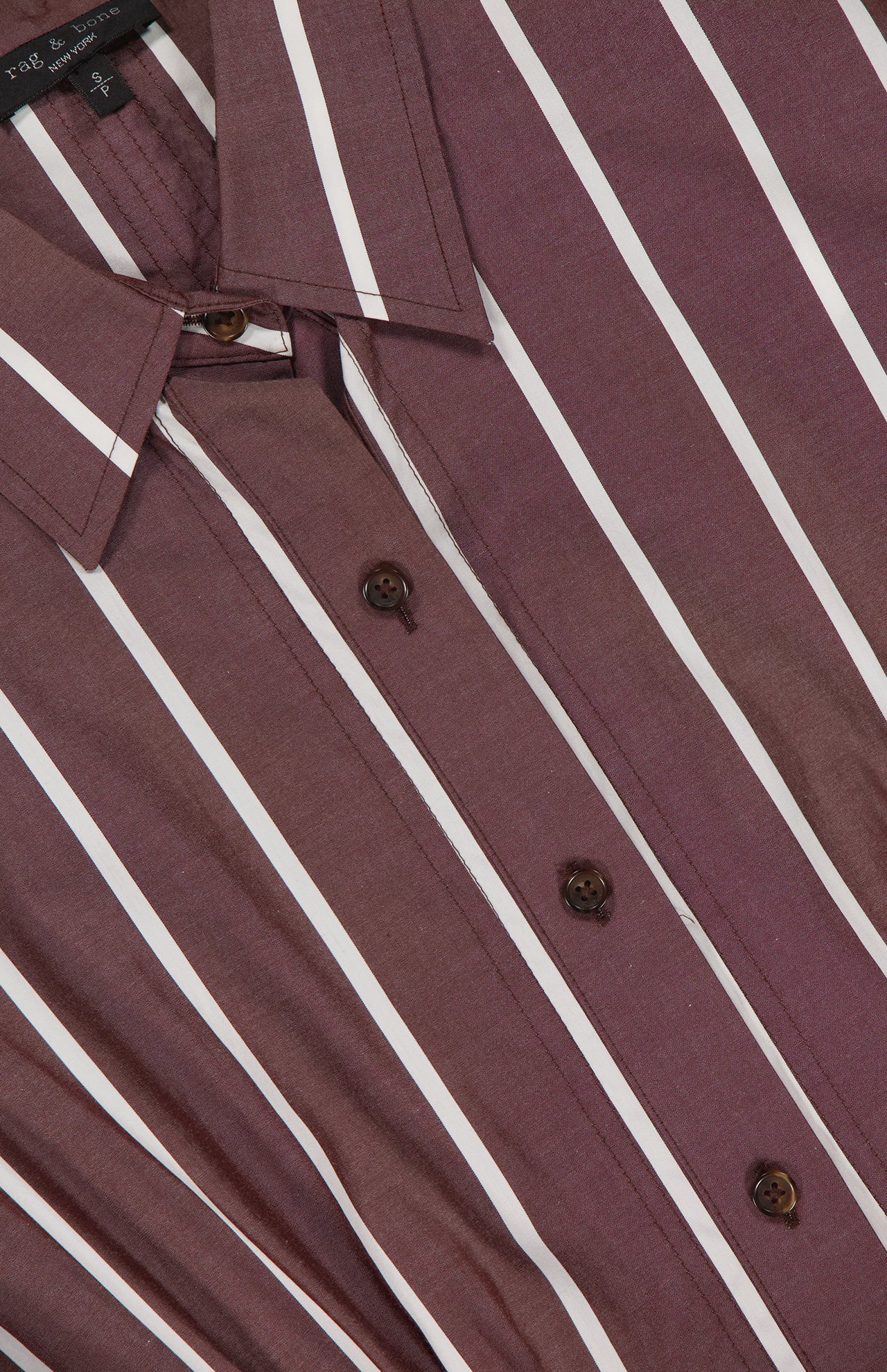 A close-up of the RAG & BONE Taylor Stripe Mini Dress, featuring maroon fabric with vertical white stripes, brown buttons, and a pointed collar. The smooth dress is neatly arranged for display.