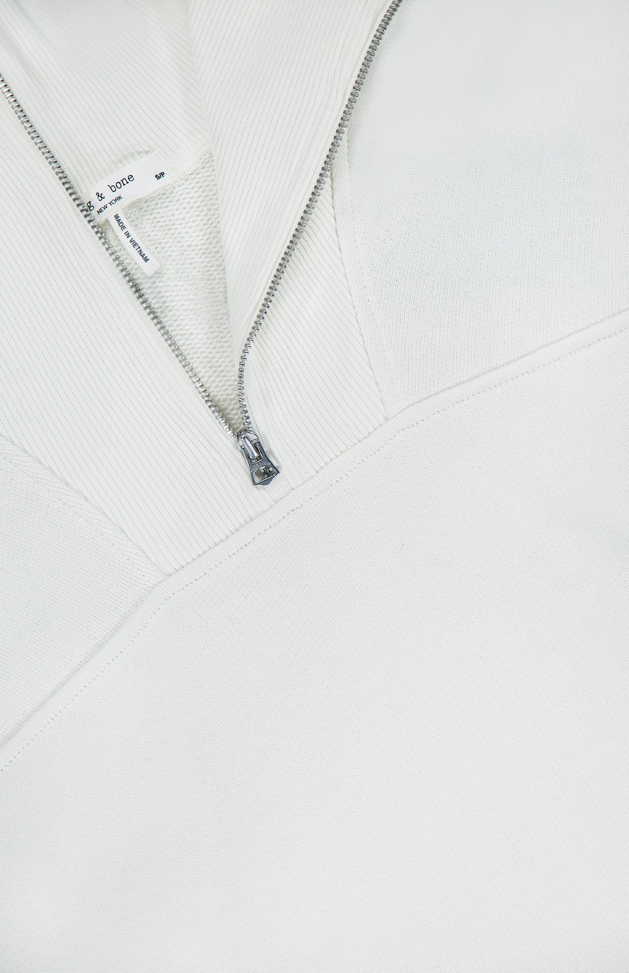 Close-up of the RAG & BONE Vintage Terry Half Zip Muscle Tank Top in white, featuring a silver zipper, ribbed collar detail, small interior tag, and a cropped fit for a modern athleisure vibe.