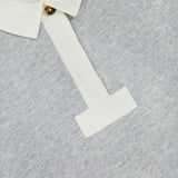 A close-up of the RAG & BONE Vintage Terry Oversized Polo Sweatshirt shows its light gray cotton-blend fabric, white collar and placket with a single brown button, soft texture, and visible brand tag inside the collar.