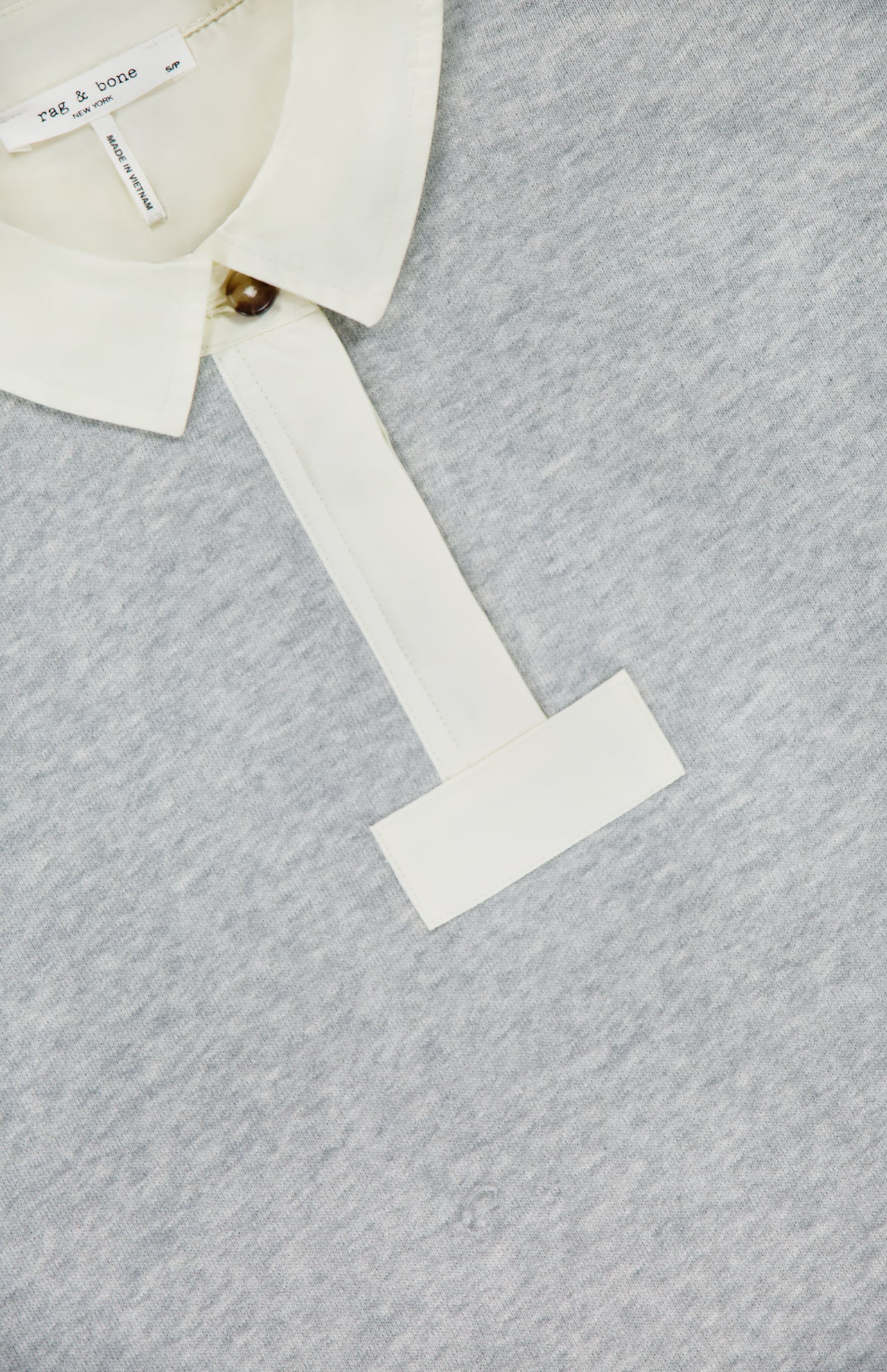 A close-up of the RAG & BONE Vintage Terry Oversized Polo Sweatshirt shows its light gray cotton-blend fabric, white collar and placket with a single brown button, soft texture, and visible brand tag inside the collar.