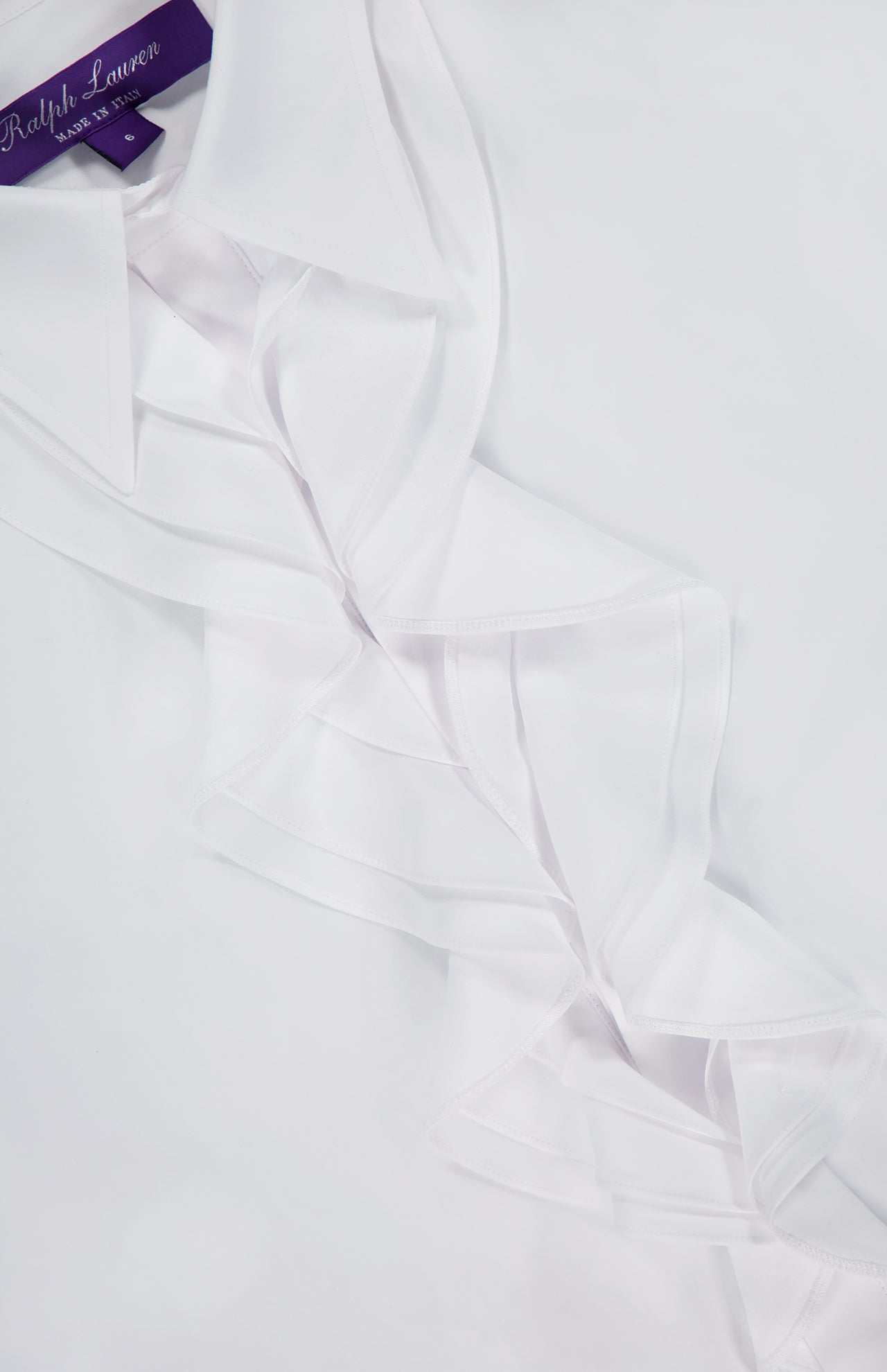 Close-up of the Addison Button Front Shirt by RALPH LAUREN COLLECTION, crafted in Italy from cotton broadcloth with a ruffle trim front and a purple Ralph Lauren label inside the collar.