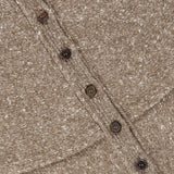 Close-up of the RALPH LAUREN COLLECTION Cashmere Turtleneck Cardigan Sweater in beige, highlighting its speckled knit texture, diagonal row of brown buttons, and visible stitching on the fabric.