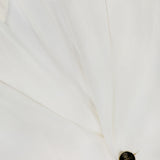Close-up of the Classic Linen Parker Blazer by RALPH LAUREN COLLECTION, an off-white piece with two pockets, a lapel, and a single dark crest-embossed button. The linen fabric looks smooth and crisp.