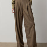 A person is wearing the Fine Wool Standard Pants from RALPH LAUREN COLLECTION—relaxed fit, wide-leg, high-waisted brown trousers in stretch-wool with pleats—paired with an olive green long-sleeve shirt. The photo is cropped below the shoulders, focusing on the lower body.