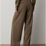 A person wearing the RALPH LAUREN COLLECTION Fine Wool Standard Pants in a relaxed, wide-leg brown style and an olive-green blouse stands with their back to the camera against a neutral background.
