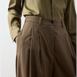 A person wears RALPH LAUREN COLLECTION Fine Wool Standard Pants in brown, a high-waisted, wide-leg style with a relaxed fit, paired with an olive green button-up shirt tucked in. One hand rests in the pants pocket. The image is cropped from the shoulders to mid-thigh.
