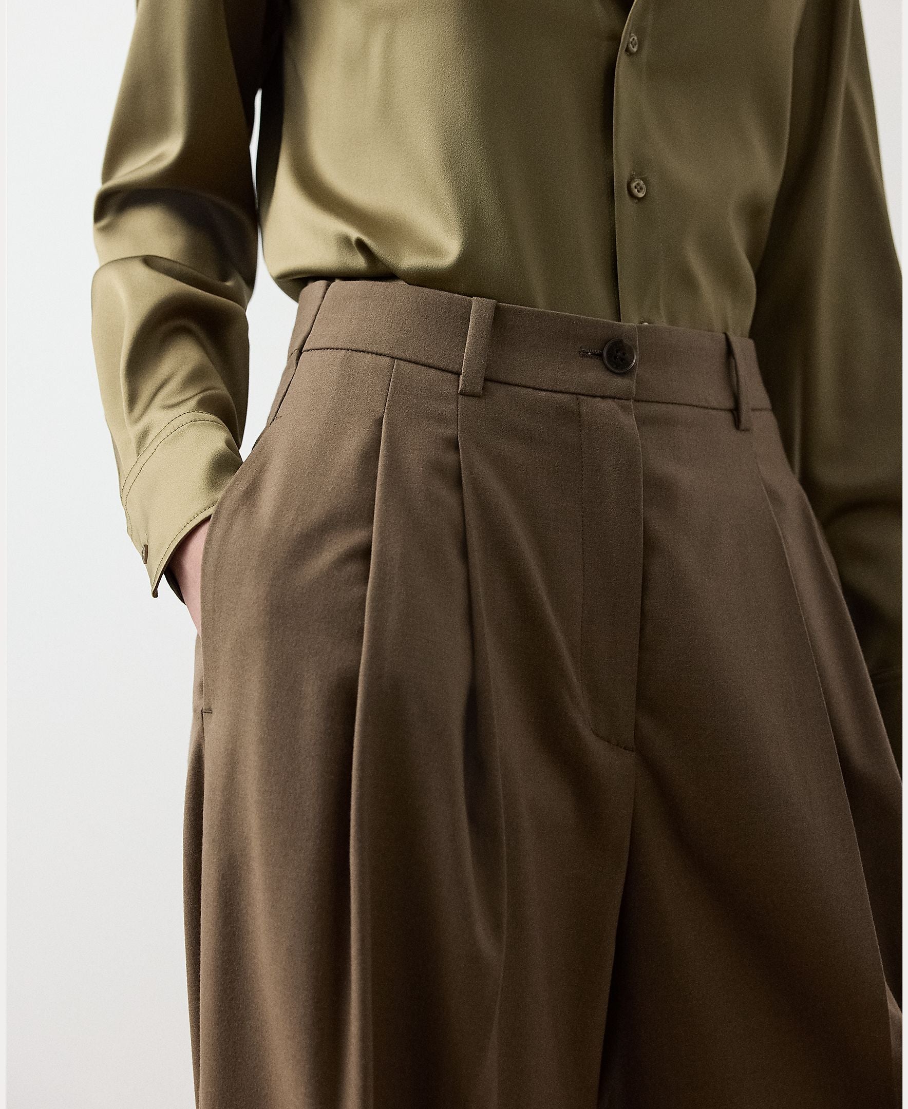A person wears RALPH LAUREN COLLECTION Fine Wool Standard Pants in brown, a high-waisted, wide-leg style with a relaxed fit, paired with an olive green button-up shirt tucked in. One hand rests in the pants pocket. The image is cropped from the shoulders to mid-thigh.