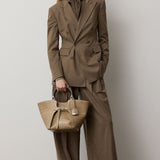 A woman in a brown double-breasted blazer and relaxed fit RALPH LAUREN COLLECTION Fine Wool Standard Pants holds a textured beige handbag.
