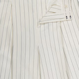The Harlo Pleated Stripe Suit Pants by RALPH LAUREN COLLECTION feature a carrot silhouette in off-white with thin black pinstripes, crafted from pleated cotton-blend suiting and shown partially unbuttoned to reveal detailed inner buttons.