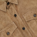 A close-up of the Landry Lightweight Suede Long Sleeve Shirt from the RALPH LAUREN COLLECTION showcases its light brown suede fabric, black buttons, and flap chest pockets. The visible collar tag features "Ralph Lauren" in white script on a purple background, emphasizing the refined details of this luxury shirt.