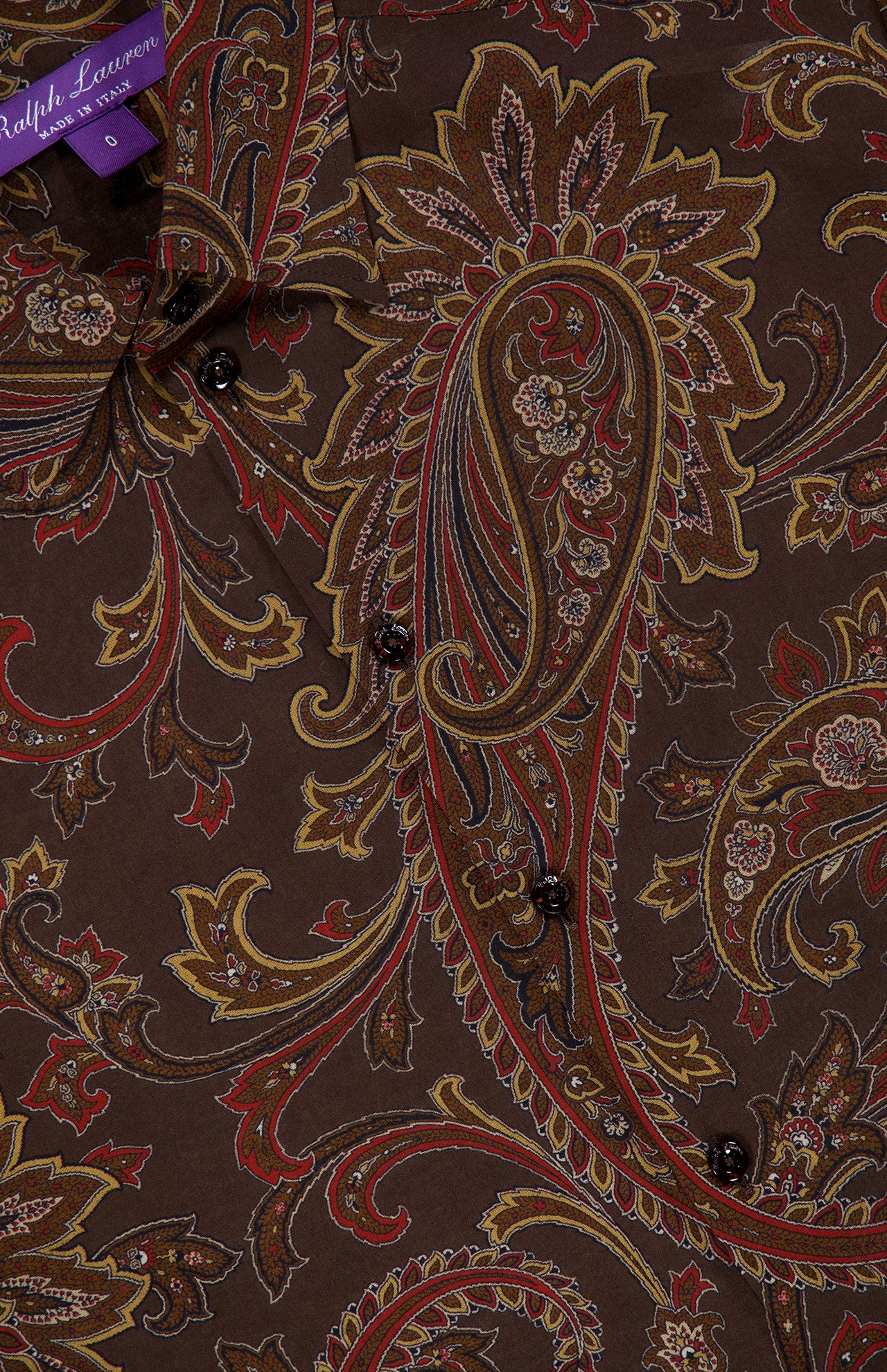 Close-up of a brown Paisley Collared Long Sleeve Blouse by RALPH LAUREN COLLECTION, featuring a paisley pattern in shades of red, yellow, and beige. Several black buttons line the front, making this blouse a versatile addition to your fall wardrobe.