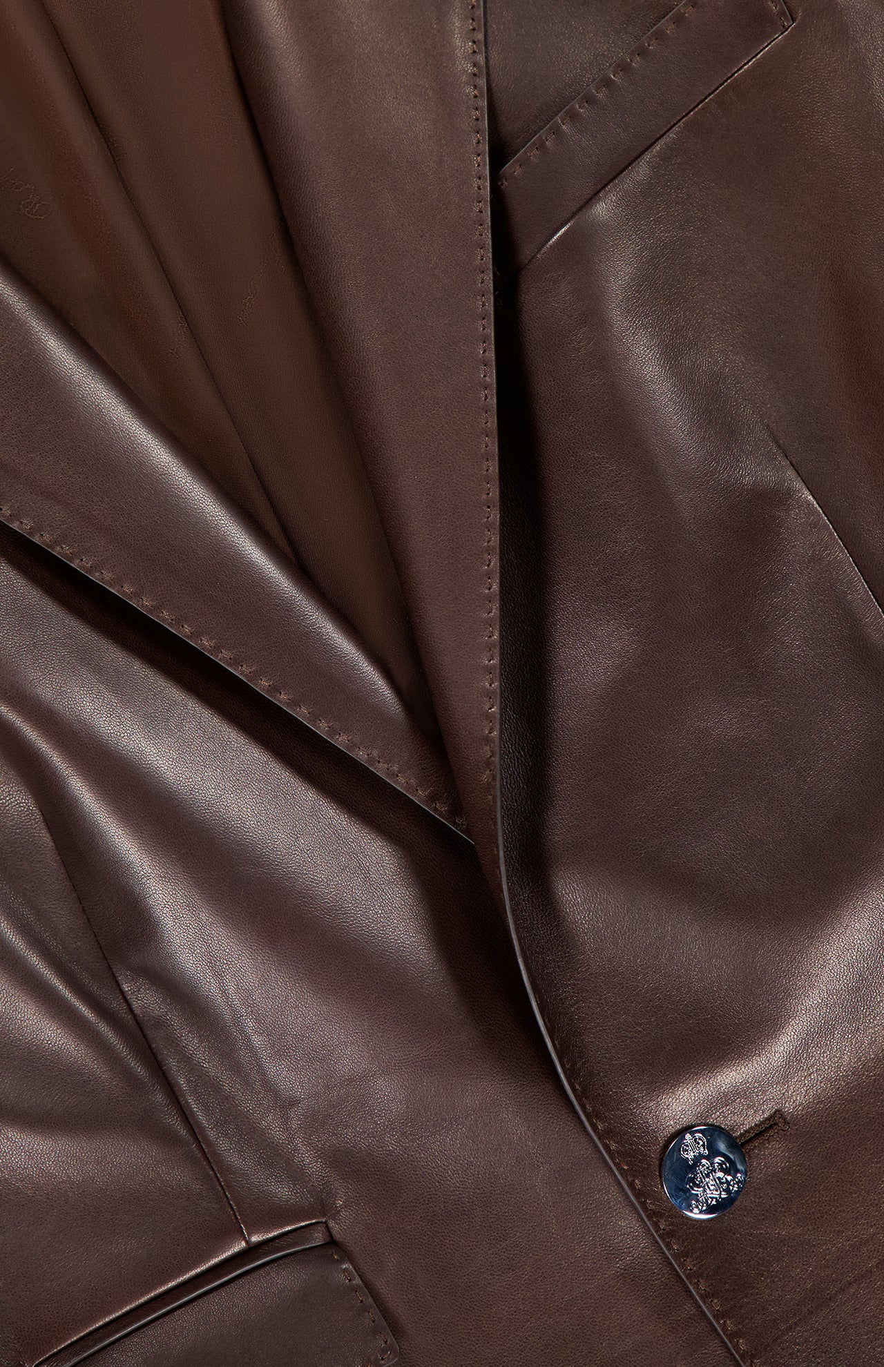 Close-up of the Parker Leather Slim Fit Blazer by RALPH LAUREN COLLECTION, showcasing its smooth chocolate brown leather, precise stitching, smart pocket design, and a single glossy black button.