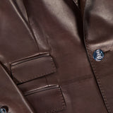 Close-up of the Parker Leather Slim Fit Blazer by RALPH LAUREN COLLECTION, featuring chocolate brown smooth, glossy leather, sharp stitching, two flap pockets, and dark buttons on the sleeve and front.