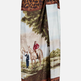 The Scenic Silk Twill Pencil Skirt from RALPH LAUREN COLLECTION showcases a vibrant print of two people and two horses by a river, elegantly framed with a brown and black leopard print border. Expertly crafted in Italy, this unique piece combines exquisite artistry with luxurious silk twill fabric.