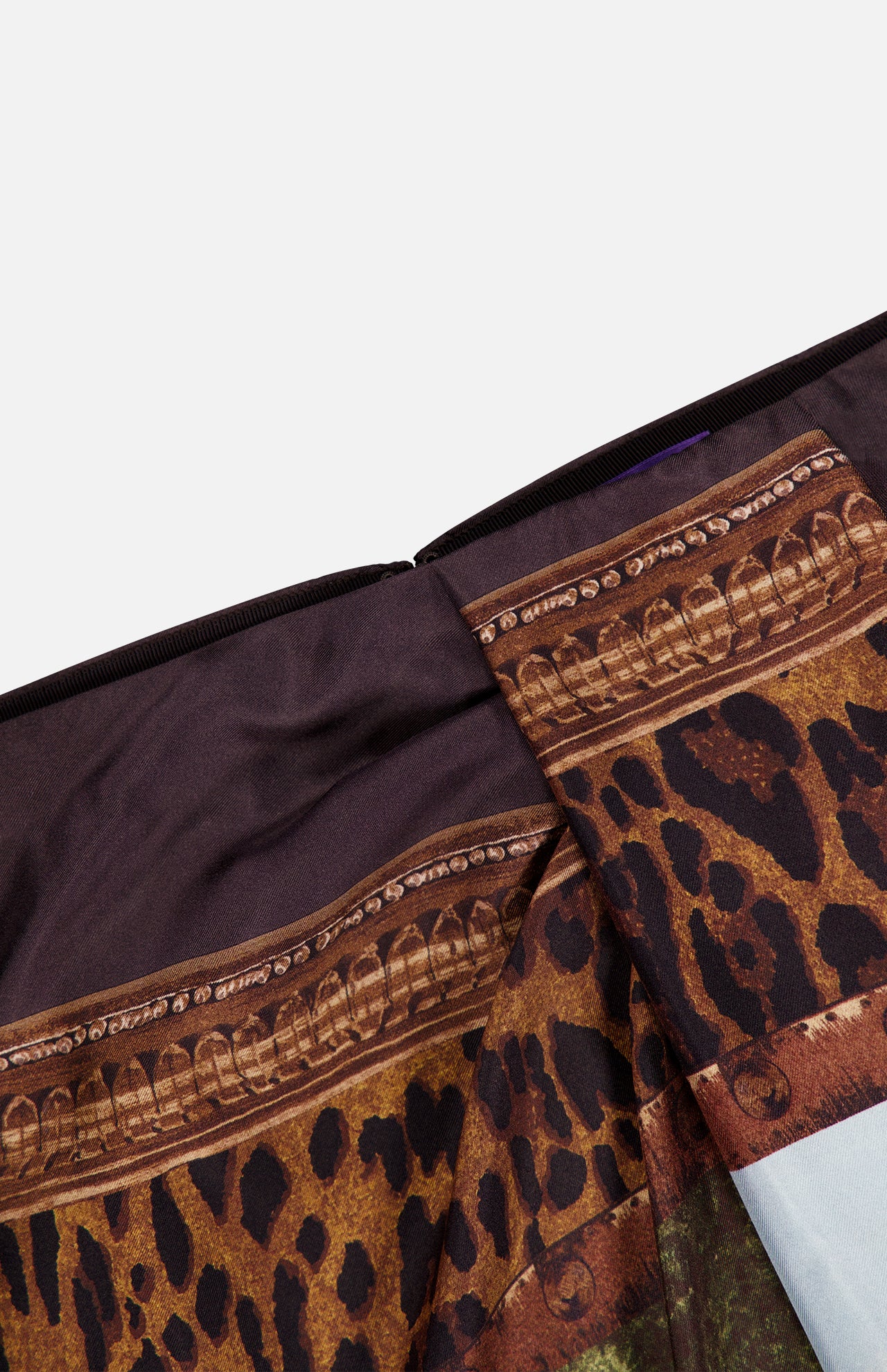 Close-up of the Scenic Silk Twill Pencil Skirt by RALPH LAUREN COLLECTION, featuring a brown and black leopard print, ornate gold decorative trim, and dark brown silk twill fabric. The image highlights a folded seam detail against a plain white background—showcasing the luxurious Italian craftsmanship of this designer skirt.