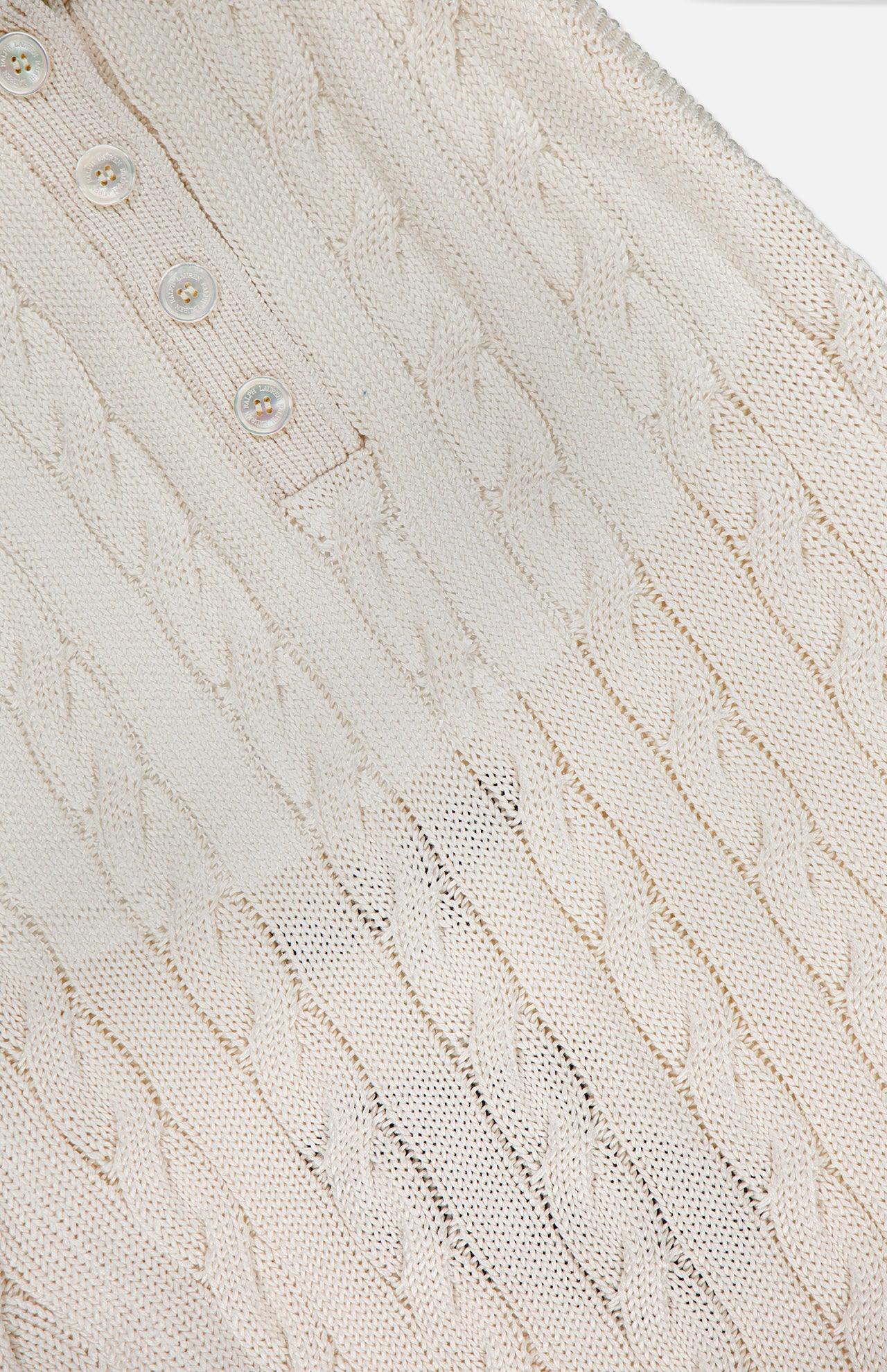 Close-up of the RALPH LAUREN COLLECTION Sleeveless Halter Polo Pullover Sweater, featuring a cream-colored cableknit texture and four pearl-like buttons on the collar—a stylish, breathable option for summer layering.