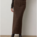 A person wears the Ralph Lauren Collection Tweed Ankle Pencil Skirt—a dark brown piece styled with a front fly and pockets—paired with a black top and dark ankle boots, standing against a light background.