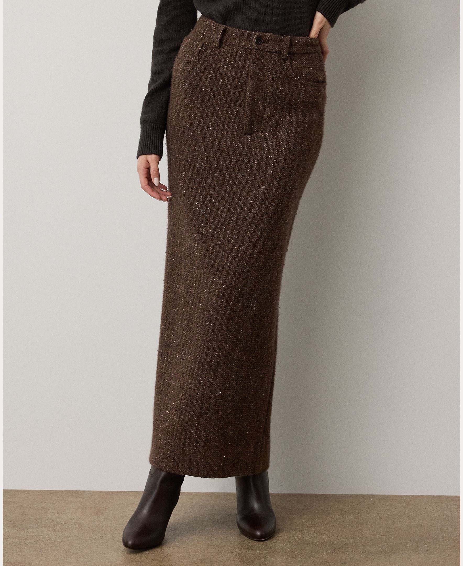 A person wears the Ralph Lauren Collection Tweed Ankle Pencil Skirt—a dark brown piece styled with a front fly and pockets—paired with a black top and dark ankle boots, standing against a light background.