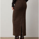 A person stands facing away from the camera against a plain background, wearing the RALPH LAUREN COLLECTION Tweed Ankle Pencil Skirt in long brown wool-cashmere with a back slit, paired with a black top and brown heeled boots.