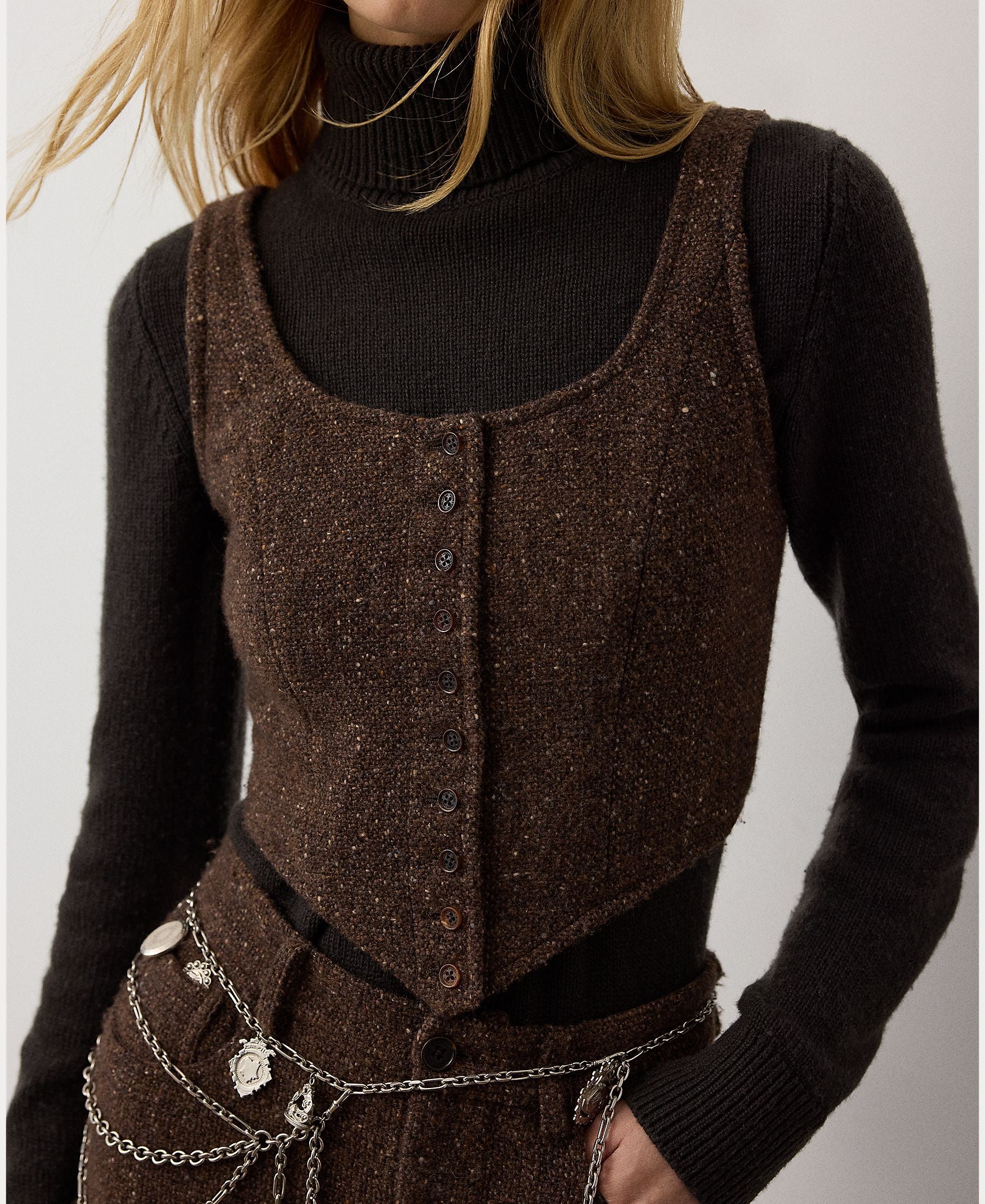 A person wearing a black turtleneck sweater layered under the RALPH LAUREN COLLECTION Tweed Scoop Neck Vest Top, paired with brown pants and a silver charm chain belt. Their face is partially out of frame.