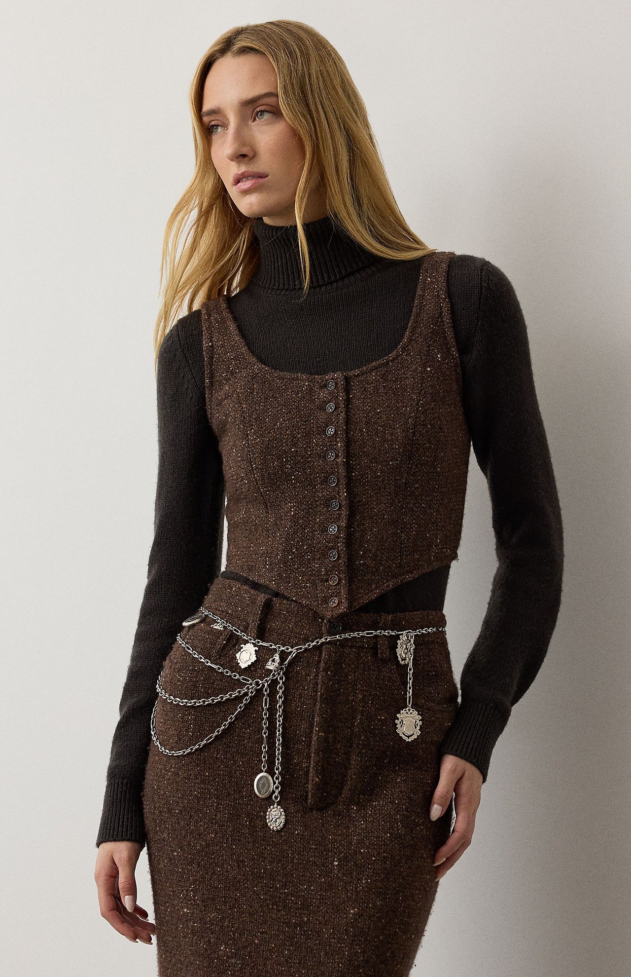 A brown RALPH LAUREN COLLECTION Tweed Scoop Neck Vest worn over a dark brown turtleneck sweater with a matching tweed skirt featuring a silver chain belt.