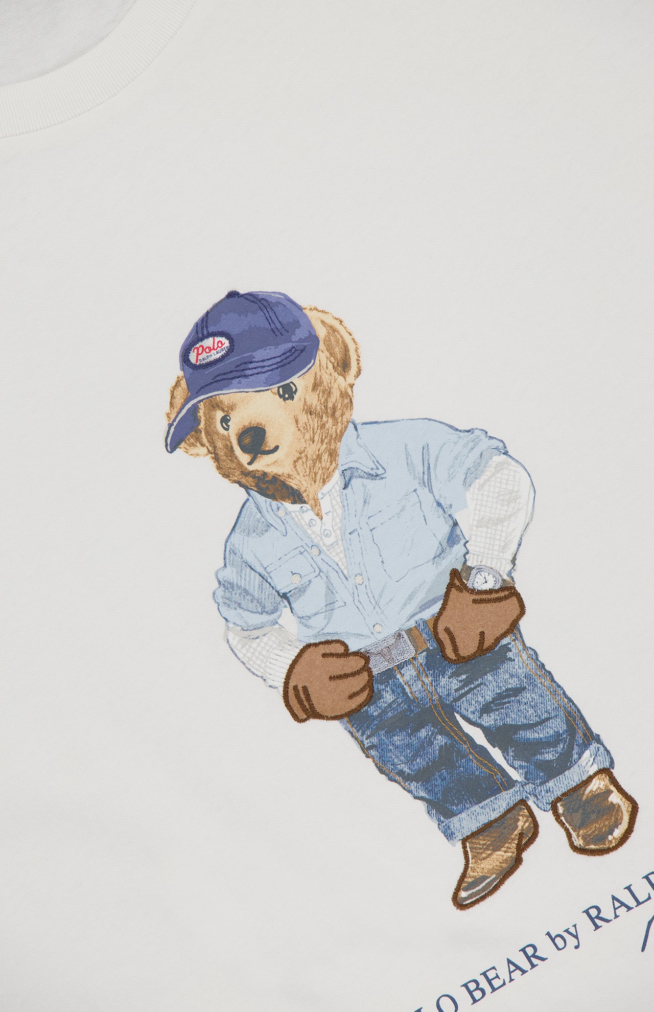 The RALPH LAUREN POLO Jersey Knit Novelty Denim Bear T-Shirt features a bear in a blue Polo cap, button-up shirt, jeans, boots, and wristwatch, detailed in embroidery on soft white cotton for timeless style.