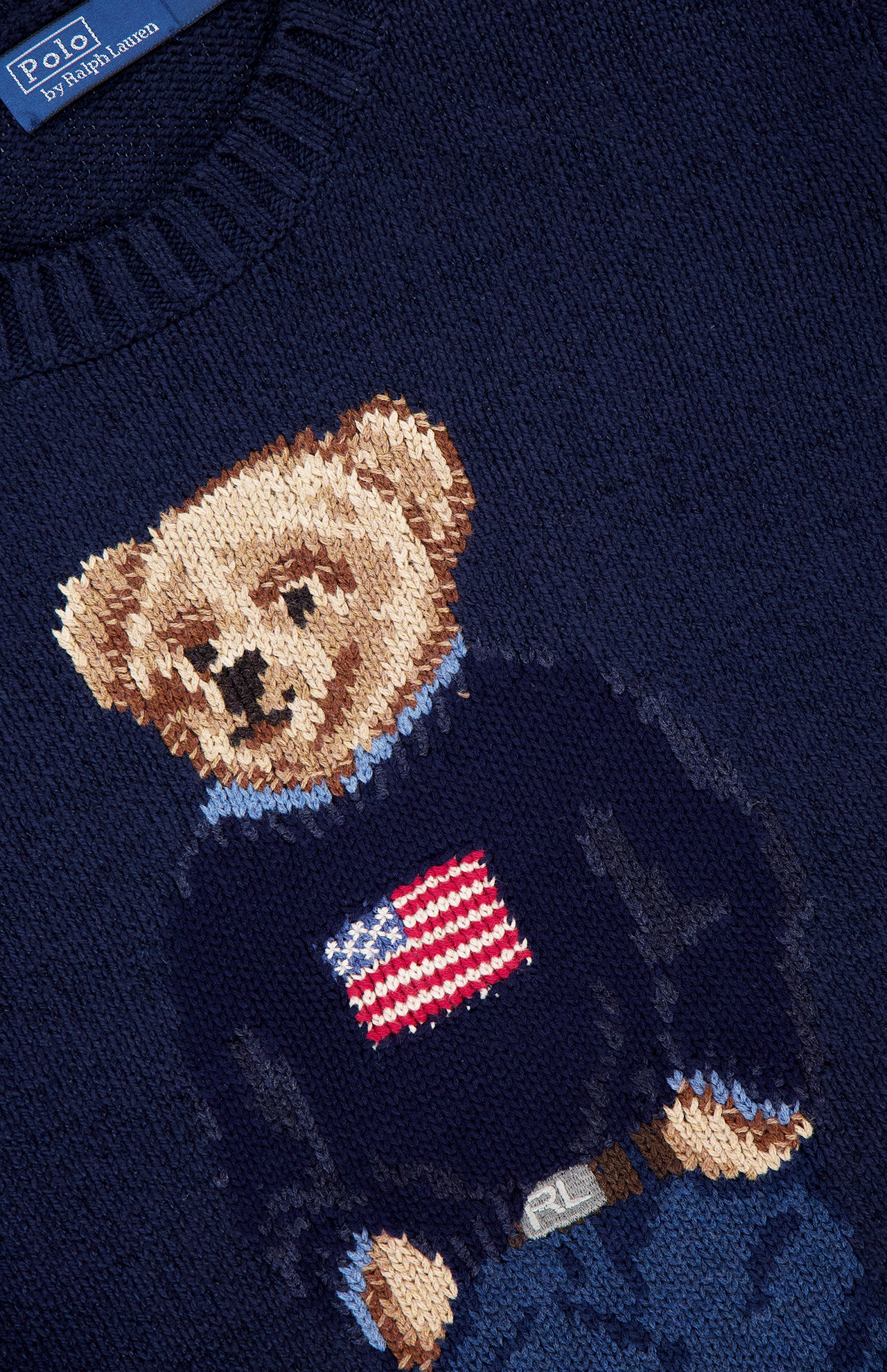 Close-up of a Cotton Linen Long Sleeve Bear Pullover Sweater by RALPH LAUREN POLO, featuring the iconic bear in an American flag sweater and blue jeans.