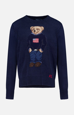 The Cotton Linen Long Sleeve Bear Pullover Sweater by RALPH LAUREN POLO features a bear in a flag sweater, blue jeans, and brown shoes, with "RL" initials on the lower front corner.