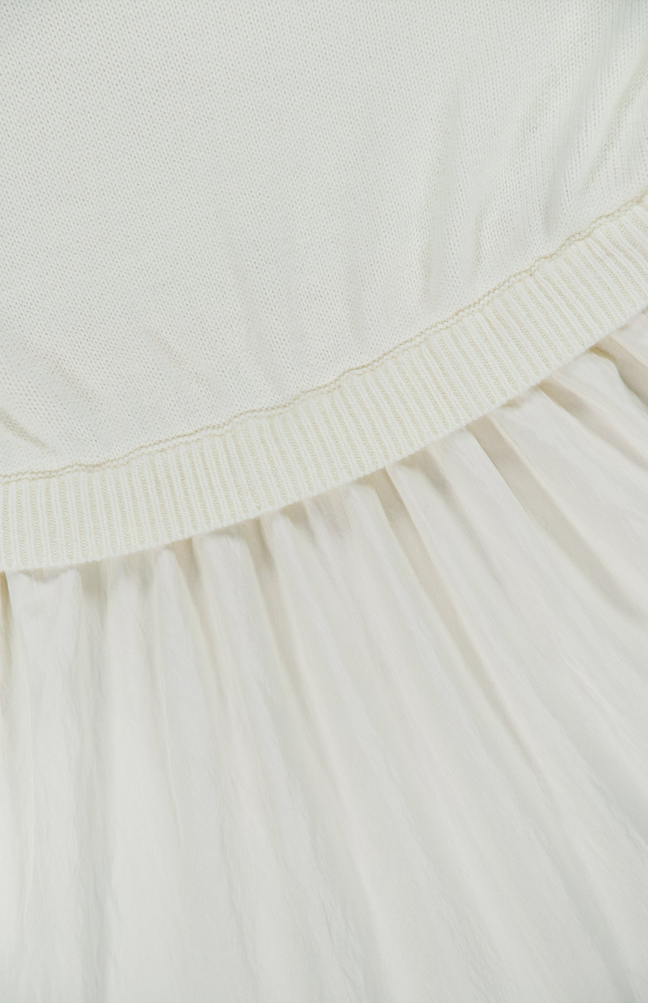 Close-up of a white knit bodice attached to an off-white pleated skirt in Italian carded-wool on a Ralph Lauren Polo Crepe Woven Turtleneck A-Line Dress.