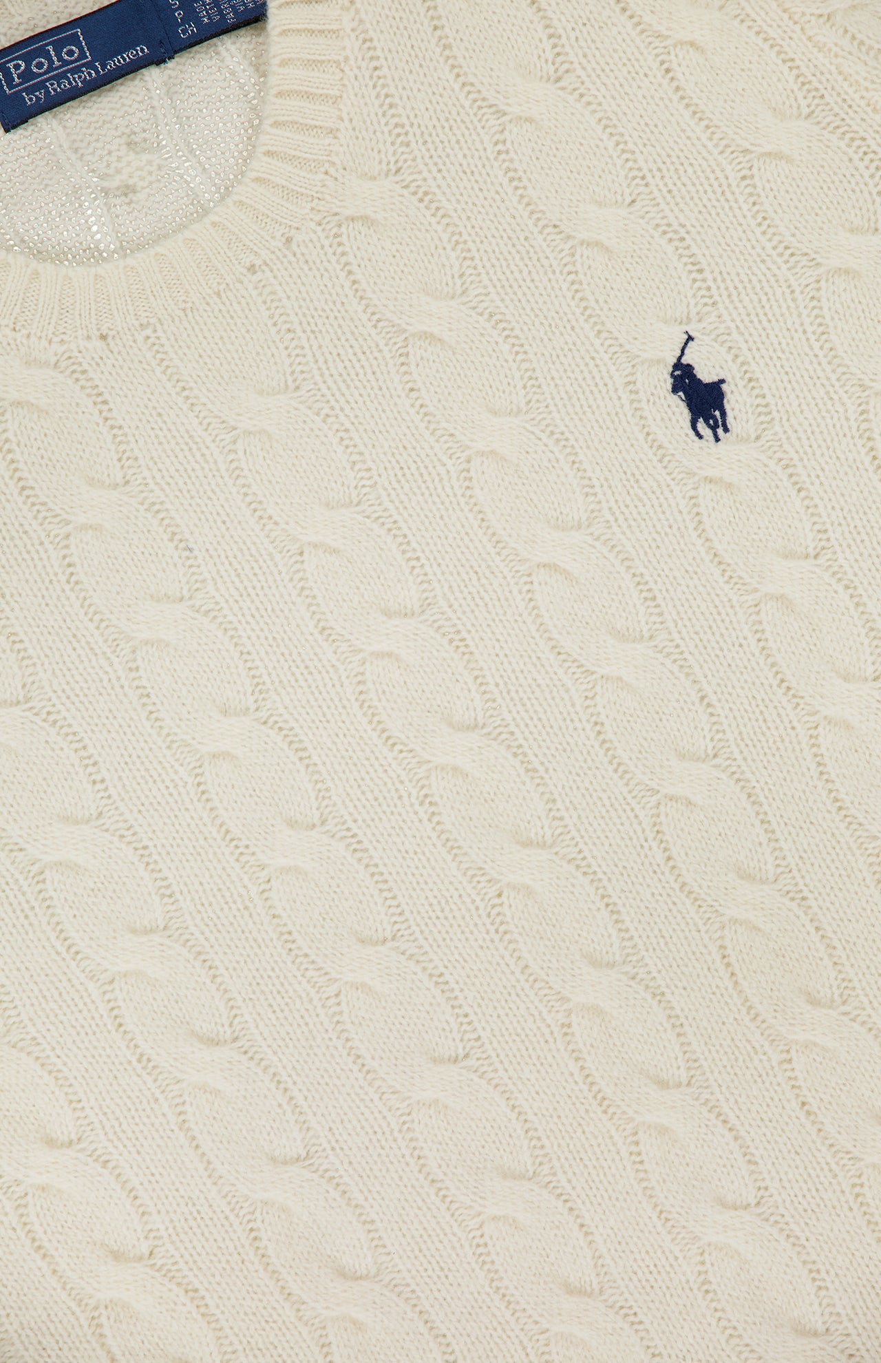 Close-up of the Julianna Long Sleeve Pullover Sweater by RALPH LAUREN POLO, a cream-colored cableknit crew neck with a small blue embroidered Pony logo and a blue Polo Ralph Lauren label on the chest.