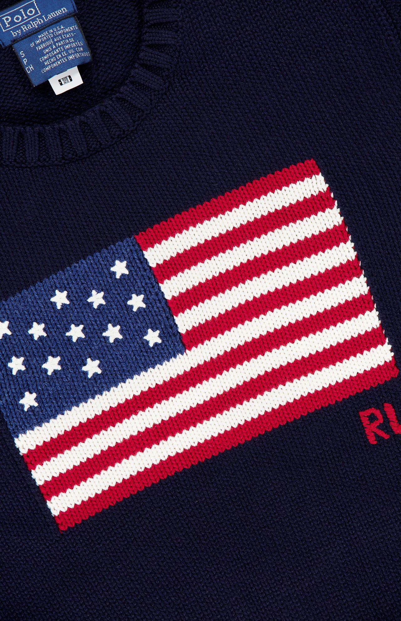 The RALPH LAUREN POLO Roving Cotton Flag Long Sleeve Pullover Sweater showcases a bold American flag and red RL letters on navy, finished with a blue label at the neck. Made in the USA.