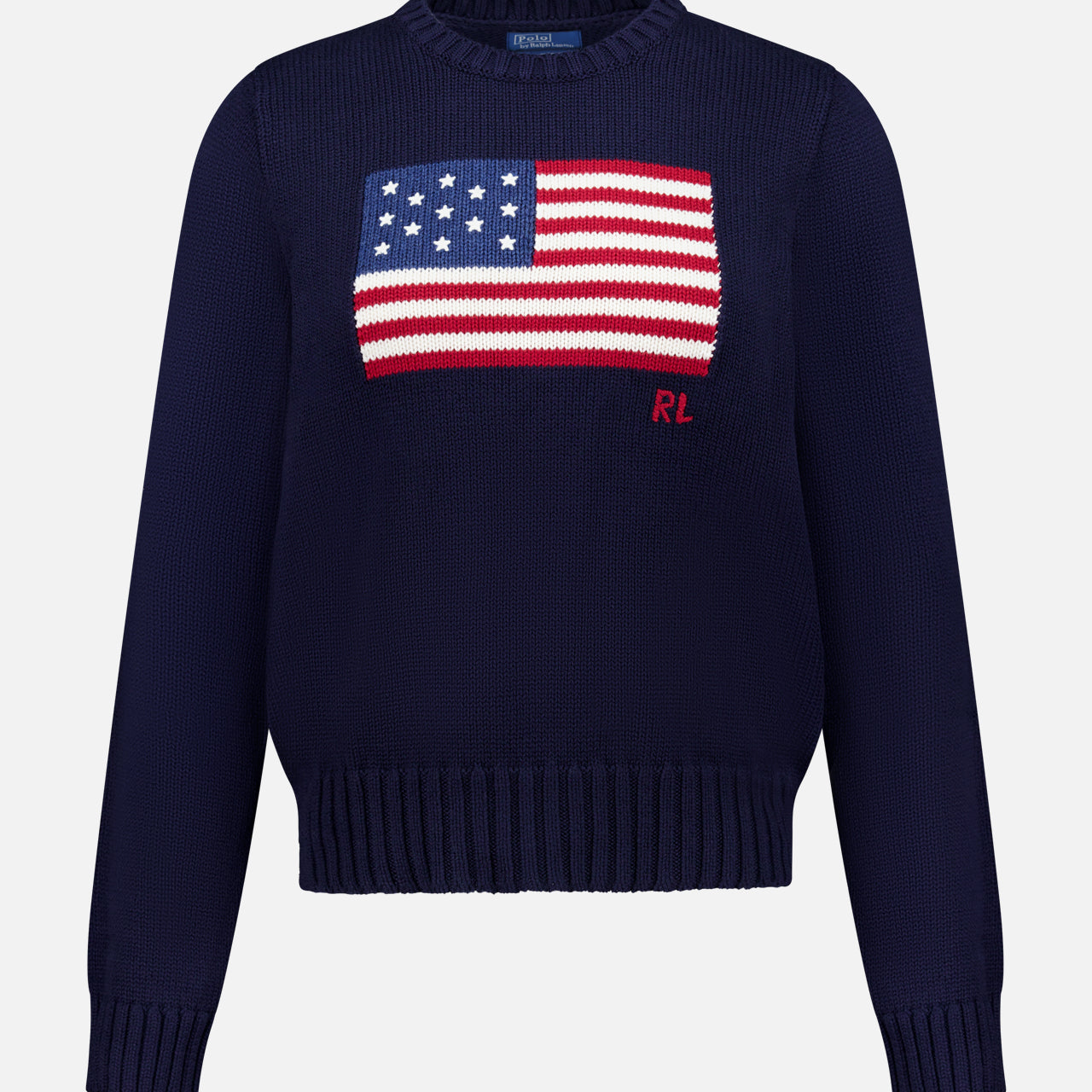 The RALPH LAUREN POLO Roving Cotton Flag Long Sleeve Pullover Sweater features a navy knit design with an American flag on the chest, red RL initials below, and ribbed cuffs, hem, and collar.
