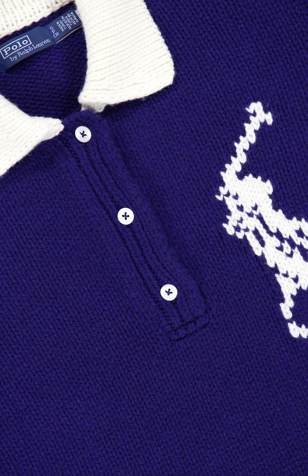 Close-up of a purple Wool Long Sleeve Polo Collar Sweater by RALPH LAUREN POLO, featuring a white collar, three white buttons, and a partial white polo player logo on the right side, reminiscent of the classic style found in a wool rugby shirt.