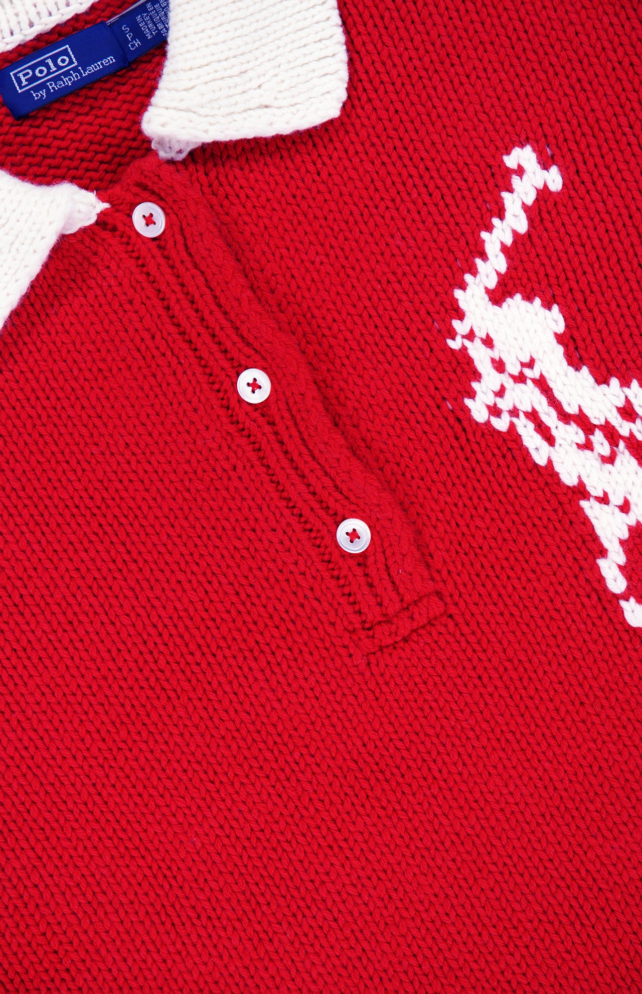 Close-up of the RALPH LAUREN POLO Wool Long Sleeve Polo Collar Sweater in red, inspired by the classic wool rugby shirt and featuring a crisp white collar, three red buttons, and a large white stitched logo of a polo player on horseback.
