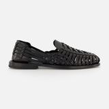 The Burnished Vacchetta Casual Loafer by RALPH LAUREN PURPLE LABEL, crafted in Italy from black woven leather with closed toe, open sides, and interlaced straps, features a flat sole and is displayed on a plain white background.