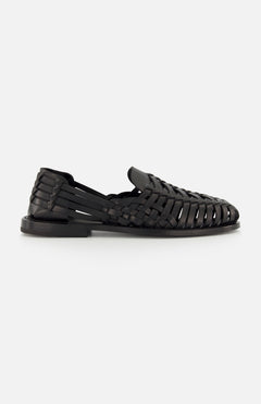 The Burnished Vacchetta Casual Loafer by RALPH LAUREN PURPLE LABEL, crafted in Italy from black woven leather with closed toe, open sides, and interlaced straps, features a flat sole and is displayed on a plain white background.