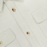 Close-up of the Calloway Suede Knit Overshirt by RALPH LAUREN PURPLE LABEL, featuring a white button-up design with two chest pockets, gold-tone buttons, and visible stitching. The edge of the signature purple label is visible inside the collar, showcasing Ralph Lauren Purple Label’s renowned sophistication and dedication to Italian craftsmanship.