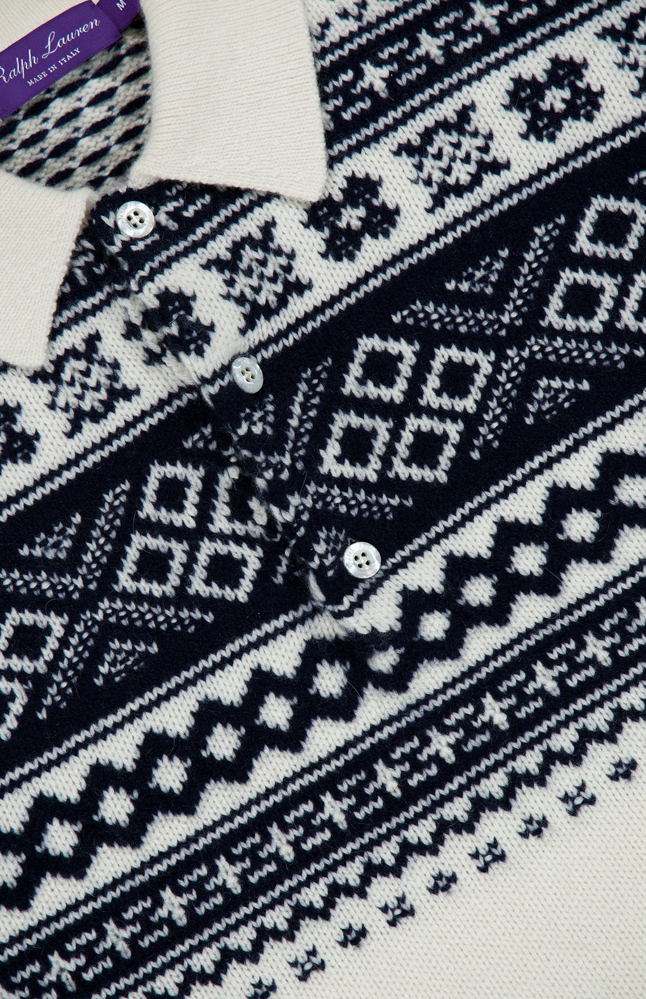 Close-up of the RALPH LAUREN PURPLE LABEL Cash Holiday Pattern Polo Sweater in cream, featuring navy blue Nordic-inspired geometric designs and three Mother of Pearl buttons on the front placket.