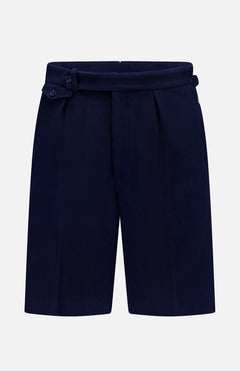 The Cashmere Herringbone Pleated Tennis Short by RALPH LAUREN PURPLE LABEL is crafted from navy blue Italian herringbone mesh fabric and features front pleats along with an adjustable side tab with buttons, shown against a plain white background.