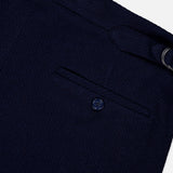Close-up of the Cashmere Herringbone Pleated Tennis Short by RALPH LAUREN PURPLE LABEL, featuring navy blue textured fabric with a buttoned trouser pocket and a metal ring detail on the waistband, evoking classic Italian tailoring, set against a white background.