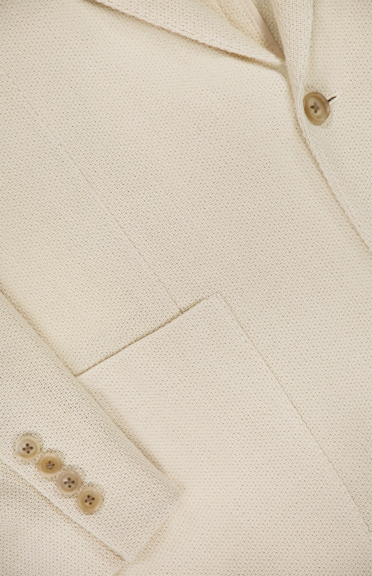 Close-up of the Cotton Panama Weave Double Breasted Sportcoat by RALPH LAUREN PURPLE LABEL—cream-colored cotton with lapel, chest pocket, and brown cuff buttons; crafted in Italy.