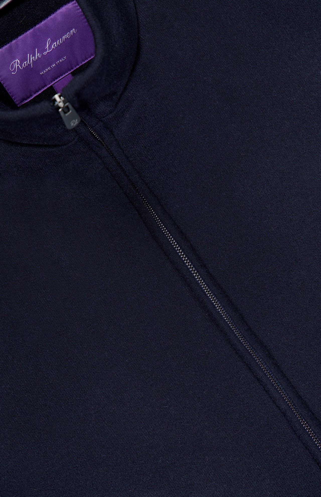 Close-up of the Double Faced Cashmere Felton Bomber Jacket, a luxury navy piece by RALPH LAUREN PURPLE LABEL, showcasing a prominent zipper and a purple Ralph Lauren label sewn inside the collar.