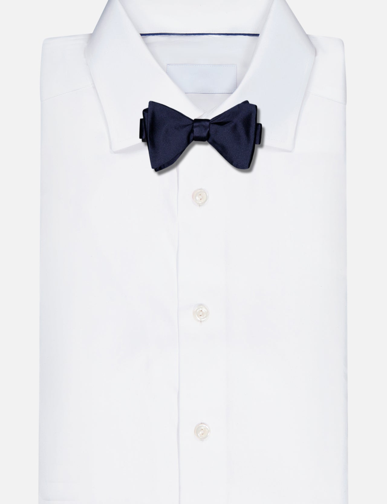 A Formal Satin Bow Tie by RALPH LAUREN PURPLE LABEL in dark navy is elegantly attached to a neatly folded white dress shirt, set against a plain light background.