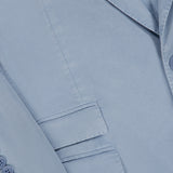 Close-up of the Garment Dyed Cotton Single Breasted Sportcoat by RALPH LAUREN PURPLE LABEL, featuring a light blue hue, a detailed lapel, a sleeve finished with three buttons, and two front flap pockets—all showcasing its vintage appeal and exquisite hand-tailored Italian craftsmanship.