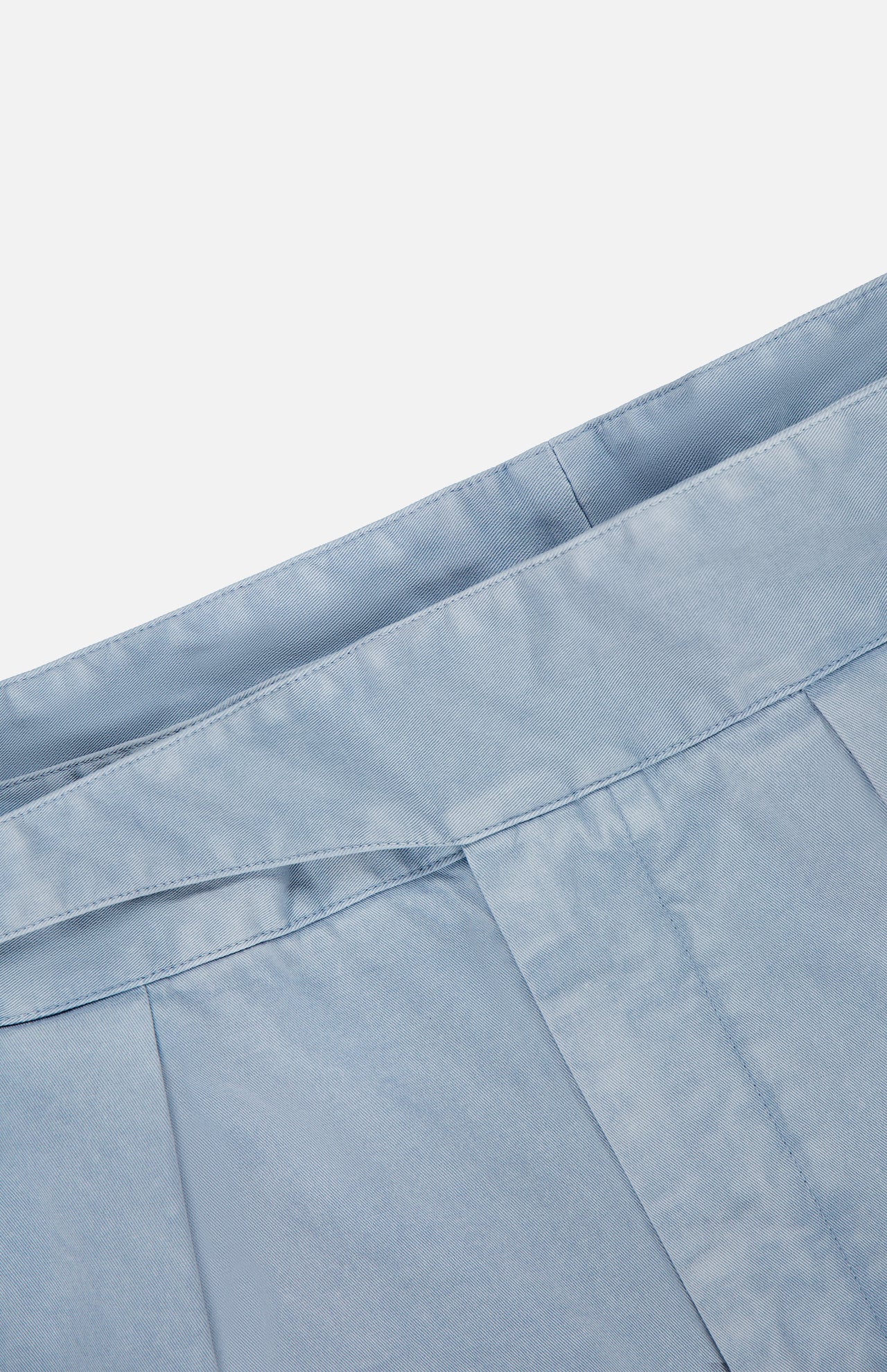 Close-up of a light blue pleated fabric from the RALPH LAUREN PURPLE LABEL Garment Dyed Cotton Trouser Pant, featuring the waistband and neatly stitched seams against a white background.