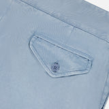Close-up of a light blue, garment-dyed cotton fabric on the RALPH LAUREN PURPLE LABEL Garment Dyed Cotton Trouser Pant, showing a single back pocket with a triangular flap and matching blue button. The visible, precise stitching highlights the refined tailoring of these stretch chino trousers for enhanced comfort.