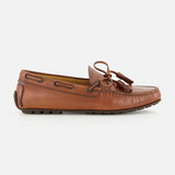 The Harold Hand Burnished Tassle Loafer by RALPH LAUREN PURPLE LABEL is crafted from premium French box calfskin in brown, showcasing classic stitching, side lacing, a front bow with tassel, and a flat rubber sole. This elegant slip-on is presented in a side profile against a plain white background.