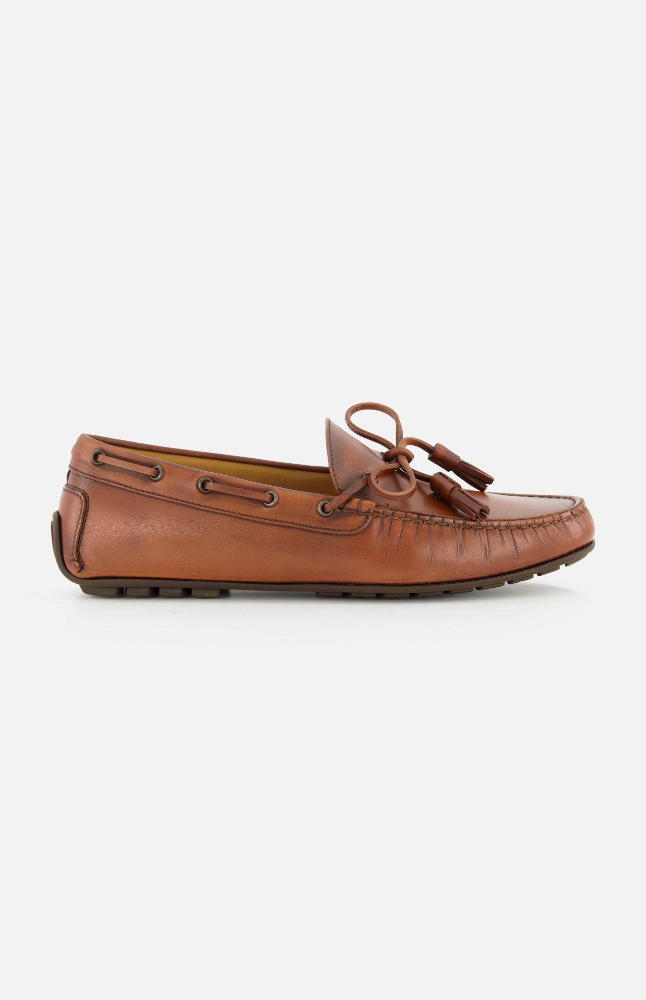 The Harold Hand Burnished Tassle Loafer by RALPH LAUREN PURPLE LABEL is crafted from premium French box calfskin in brown, showcasing classic stitching, side lacing, a front bow with tassel, and a flat rubber sole. This elegant slip-on is presented in a side profile against a plain white background.