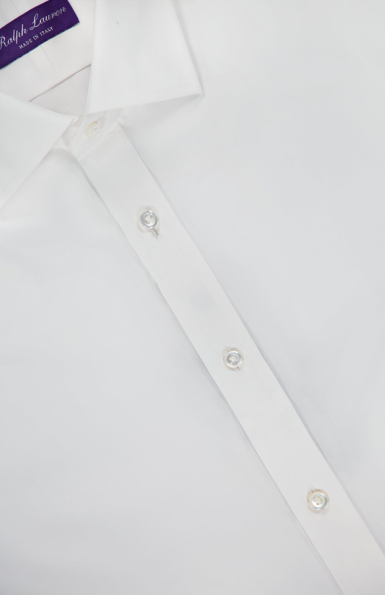 Close-up of the Journey Twill Long Sleeve Dress Shirt by RALPH LAUREN PURPLE LABEL, crafted from soft white cotton twill with pearl-like buttons and a visible collar. A purple label at the neck reads Ralph Lauren Made in Italy. The shirt appears clean and neatly pressed.
